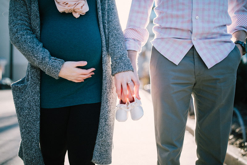 έγκυος γυναίκα με το σύντροφό της ενισχύουν τον δεσμό τους κρατώντας παιδικά παπούτσια