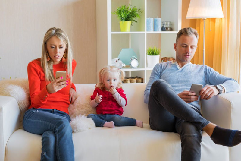 γονείς καθισμένοι στον καναπέ αγνοούν το παιδί τους και κοιτάζουν τα τηλέφωνά τους
