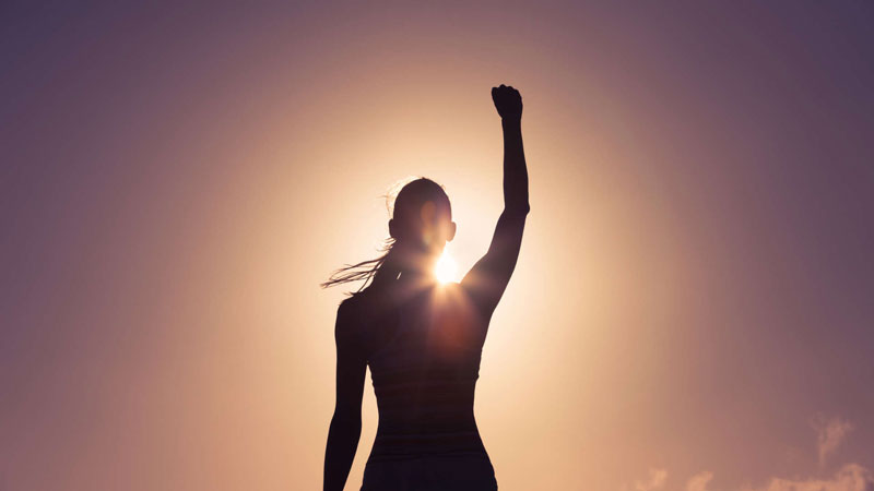 γυναίκα σηκώνει το χέρι της ψηλά με φόντο τον ήλιο