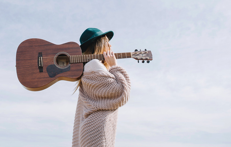γυναίκα με κιθάρα στη πλάτη αναζητά τις ψυχοθεραπευτικές προσεγγίσεις της μουσικοθεραπείας στην ψυχική υγεία