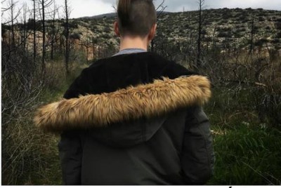 έφηβος με κοτσιδάκι και μπουφάν που βρίσκεται σε δάσος με γυρισμένη την πλάτη στην φωτογραφική κάμερα