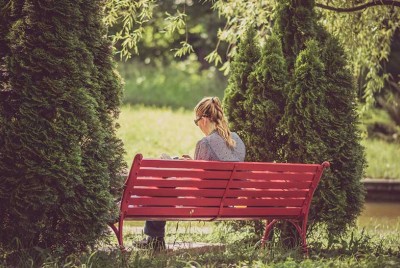 γυναίκα κάθεται μόνη σε κόκκινο παγκάκι στο πάρκο διαβάζοντας βιβλίο έχει καλές σχέσεις αφού έχει καλή σχέση με τον εαυτό της