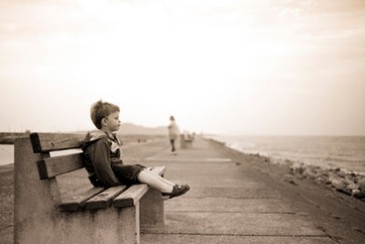 παιδί που κάθεται μόνο του και παραμελημένο σε παγκάκι κοντά στη θάλασσα