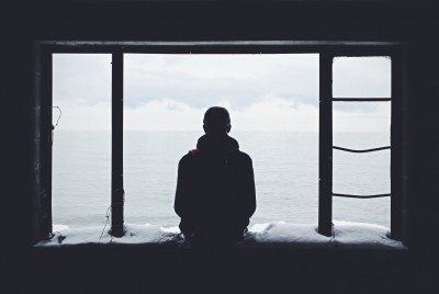 νέος άνδρας κοιτάζει τη θάλασσα καθισμένος μέσα από ένα παράθυρο