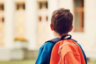 παιδί με πορτοκαλί τσάντα στον ώμο κοιτάζει το σχολείο του