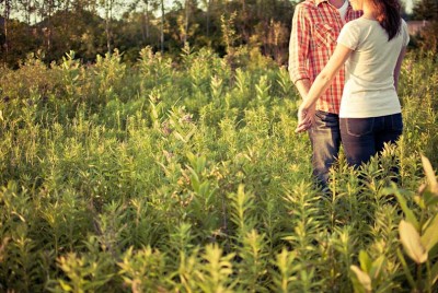 ζευγάρι κρατιέται χέρι-χέρι σε ένα χωράφι με ψηλά χόρτα