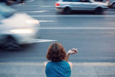 κοπέλα κοιτάζει το δρόμο με αυτοκίνητα κρατώντας τσιγάρο
