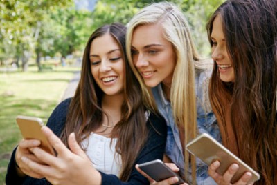 τρεις έφηβες κοπέλες κοιτάζουν τα κινητά τηλέφωνά τους