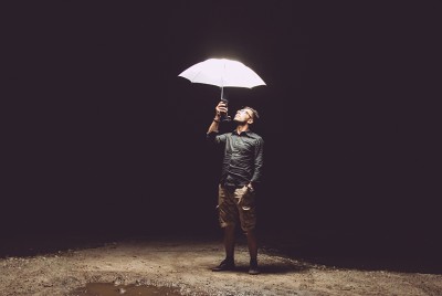 άντρας που κρατάει μία φωτεινή ομπρέλα μέσα στο σκοτάδι