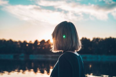 γυναίκα κοιτάει το ηλιοβασίλεμα μπροστά από μια λίμνη