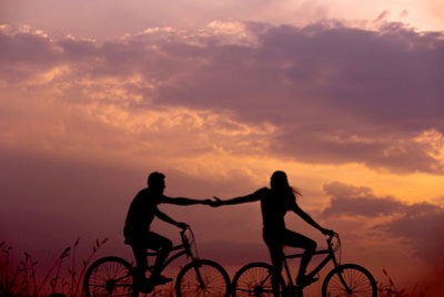 γυναίκα και άντρας πάνω σε ποδήλατα που πιάνουν τα χέρια τους