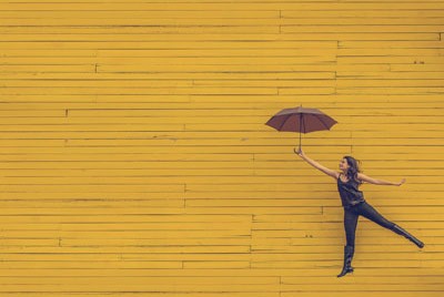 κοπέλα που κρατάει ομπρέλα μπροστά σε κίτρινο τοίχο