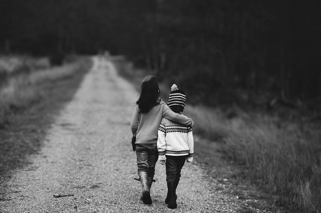 δύο παιδιά αγκαλιασμένα να περπατούν σε ένα χωματόδρομο