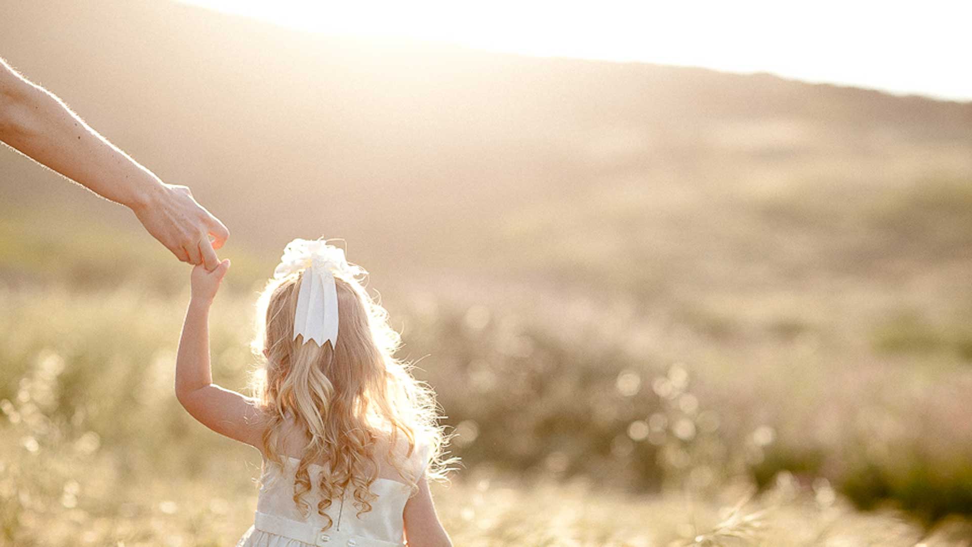 μικρό ξανθό κοριτσάκι περπατάει στη φύση κρατώντας το χέρι του γονέα της