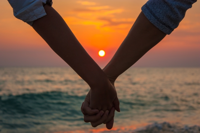 ζευγάρι κρατιέται χέρι-χέρι στο ηλιοβασίλεμα στην παραλία