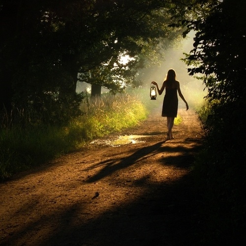 γυναίκα κρατάει μια λάμπα πετρελαίου και περπατάει σε ένα μονοπάτι στο δάσος