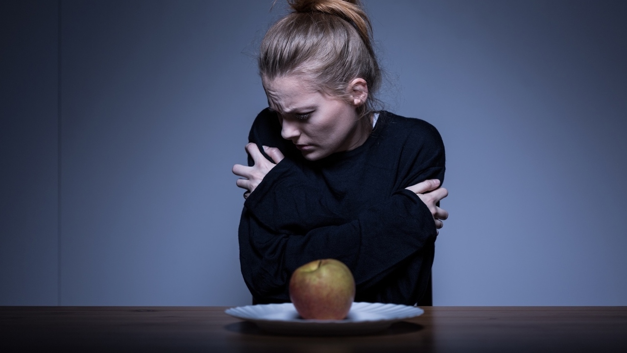 γυναίκα σφιχταγκαλιάζεται μπροστά σε ένα πιάτο με ένα μήλο