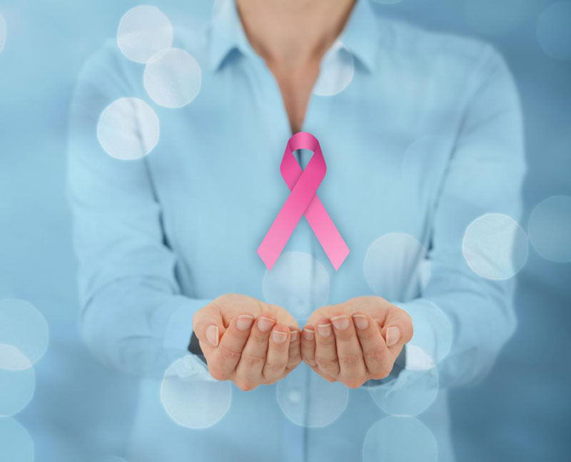 γυναίκα που εμφανίζεται από το λαιμό και κάτω με μπλε πουκάμισο να προτείνει τα χέρια σε ένα λογότυπο για τον καρκίνο του μαστού