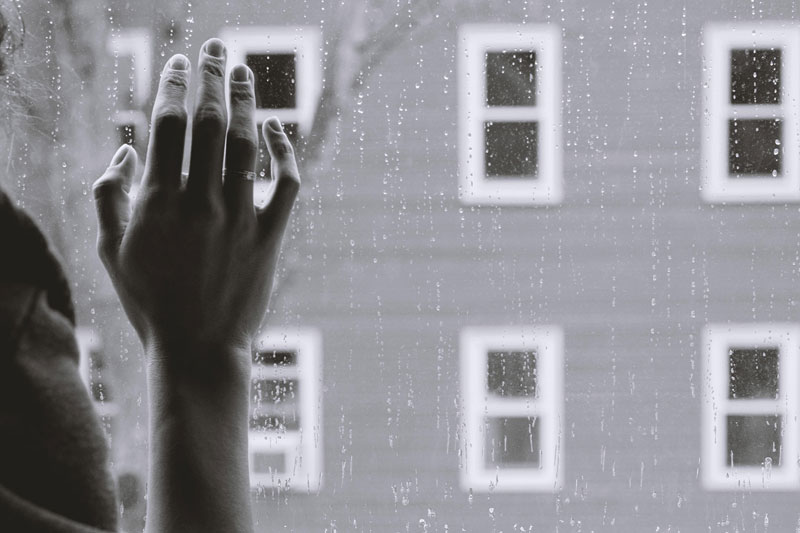 χέρι που ακουμπάει σε παράθυρο ενώ έξω βρέχει