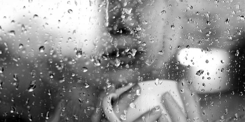 γυναίκα με κατάθλιψη που κρατά ένα φλιτζάνι μπροστά σε ένα παράθυρο με βροχή