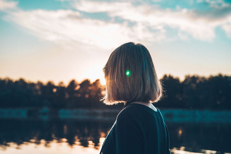 γυναίκα κοιτάει το ηλιοβασίλεμα μπροστά από μια λίμνη