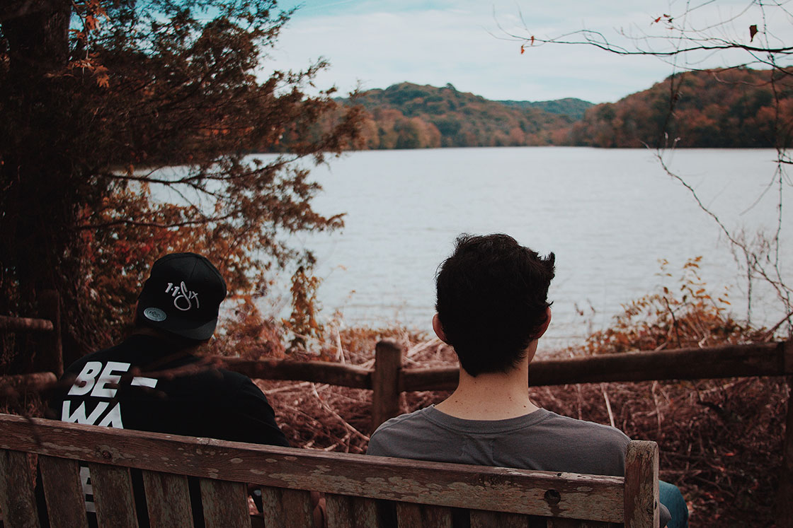 2 άντρες κάθονται σε ένα παγκάκι με θέα μια λίμνη