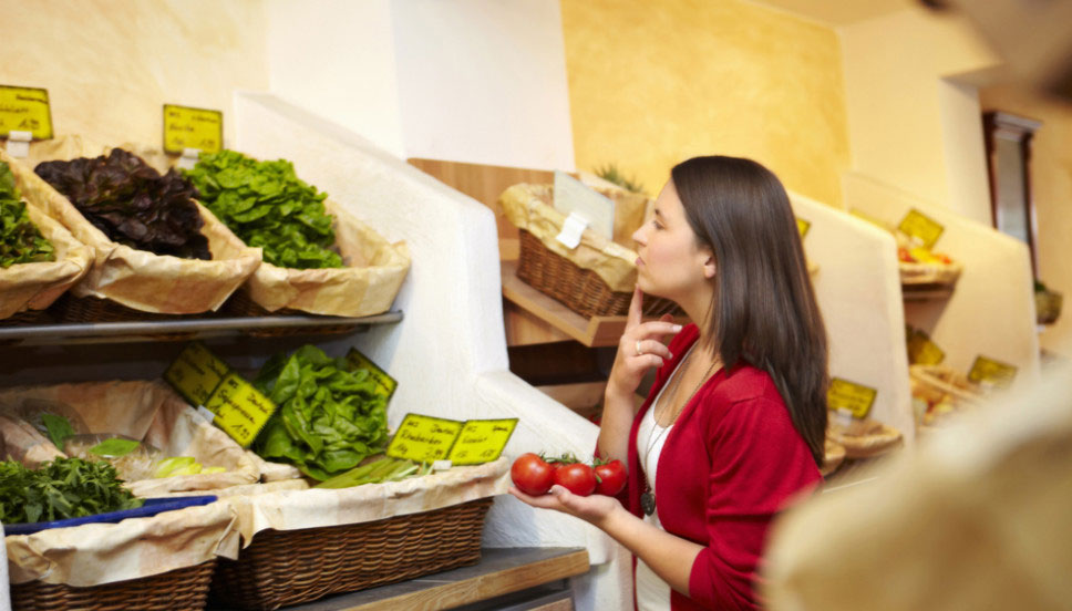 γυναίκα στο σούπερ μάρκετ σκέφτεται τι λαχανικά θα αγοράσει